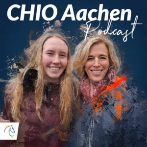 Cover of the CHIO Aachen Podcast. Two people, a mother and daughter with long, light hair, stand smiling next to each other in front of an artistically designed, dark blue background with colour accents. At the top, in large white letters, is ‘CHIO Aachen Podcast’, and at the bottom left is the colourful CHIO Aachen logo with a stylised horse's head.