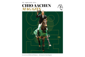 Titelblatt des „CHIO AACHEN MAGAZIN“ 2026, Ausgabe 59: Ein Springreiter in hellem Jackett reitet auf einem braunen Pferd im grünen ROLEX-Siegersattelpad direkt auf den Betrachter zu und hebt lächelnd seinen Reithelm. Der Hintergrund ist dunkelgrün mit großen, grafischen Linien und der gelben Zahl „26“. Oben stehen Titel, Jahrgang, Ausgaben- und Preisangabe, unten der Untertitel „Das Journal zum Weltfest des Pferdesports – World Equestrian Festival Magazine“ sowie ein stilisiertes Pferdekopf-Logo.